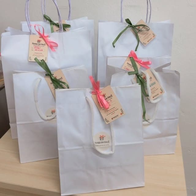 Sacolinhas brancas de papel com fita verde e rosa e a etiqueta parda da loja, prontas para entregar
